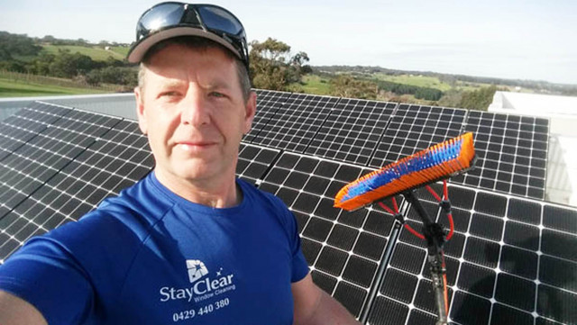Neil Beckett of Stay Clear cleaning solar panels on a residential rooftop in Mornington, Victoria, using a water-fed pole system. The image shows professional solar panel maintenance in action, with streak-free, chemical-free cleaning that helps panels p